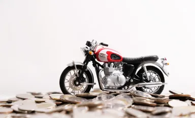 Une moto miniature posée sur un tas de pièces de monnaie