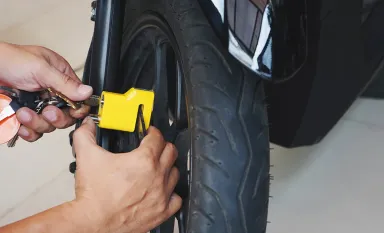 Un homme en train d'installer un antivol jaune sur la roue de sa moto