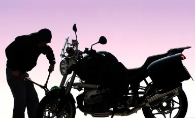 Un voleur avec une pince en train de casser l'antivol posé sur une moto