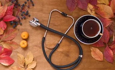 Des feuilles d'automne, un stéthoscope et une tasse de thé posés sur une table en bois