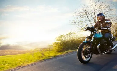 Un motard roulant sur une route avec du soleil en arrière plan