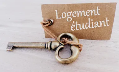 Une clé posée sur une table avec une pancarte où est inscrit "logement étudiant"