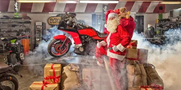 Un Père Noël posant devant une moto et des cadeaux 