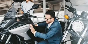 Un homme en costume en train de contrôler une moto grise avant de l'acheter