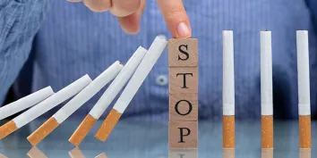 Une femme arrêtant une ligne de cigarette tombant sur un bureau avec le mot STOP écrit avec des cubes en bois