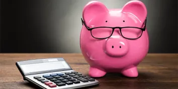 Un cochon tirelire rose à lunettes posé à côté d'une calculatrice