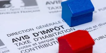Deux maisons miniatures bleue et rouge posées sur un avis d'imposition de la taxe d'habitation