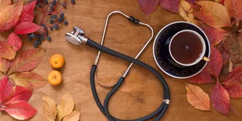 Des feuilles d'automne, un stéthoscope et une tasse de thé posés sur une table en bois