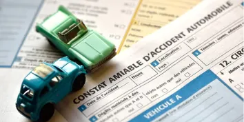 Deux voitures miniatures posés sur un exemplaire de constat amiable d'accident