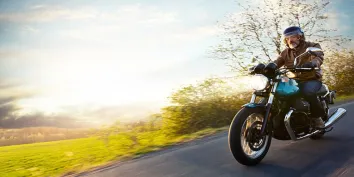 Un motard roulant sur une route avec du soleil en arrière plan
