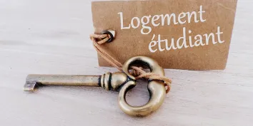 Une clé posée sur une table avec une pancarte où est inscrit "logement étudiant"