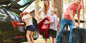 Une famille heureuse remplit le coffre de la voiture de valises avant de partir en vacances