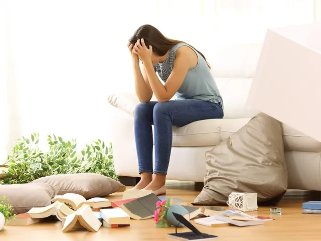 Femme assise sur un canapé dans un appartement sinistré suite à un cambriolage