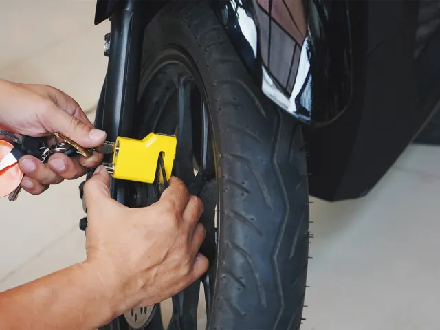 Un homme en train d'installer un antivol jaune sur la roue de sa moto