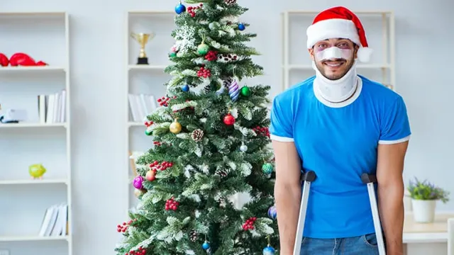 Un jeune homme avec des béquilles et portant un bonnet de père Noël devant un sapin
