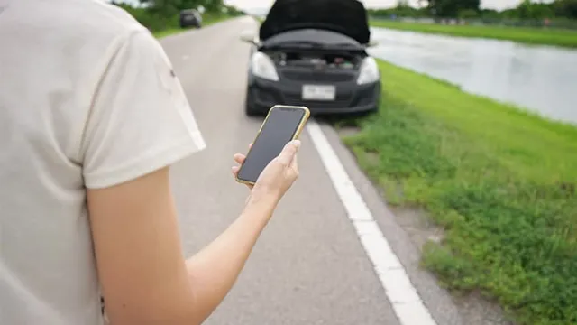 Un jeune homme téléphone à la main devant sa voiture en panne
