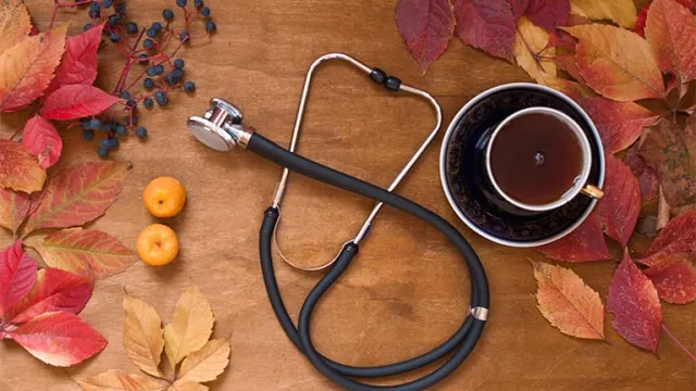 Des feuilles d'automne, un stéthoscope et une tasse de thé posés sur une table en bois