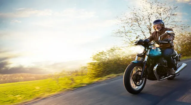 Un motard roulant sur une route avec du soleil en arrière plan