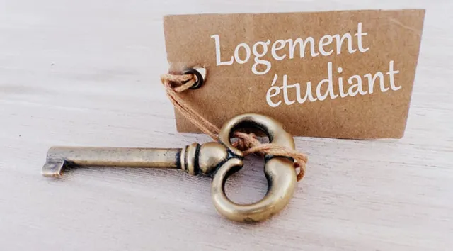 Une clé posée sur une table avec une pancarte où est inscrit "logement étudiant"