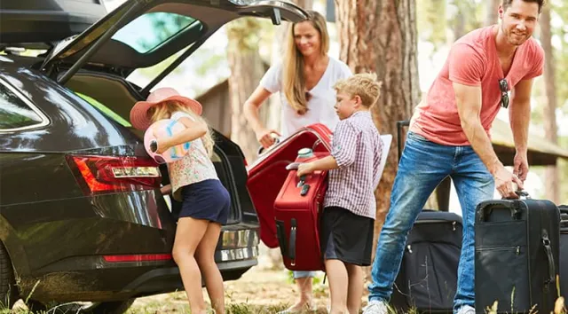 Une famille heureuse remplit le coffre de la voiture de valises avant de partir en vacances