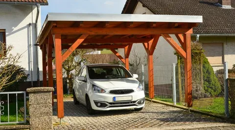 Une voiture blanche sous un carport en bois